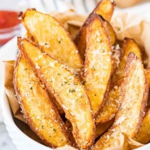 Quartiers de pomme de terre à la friteuse à air dans un bol blanc, garnis de Parmigiano