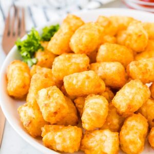 Tater Tots cuits à l'air sur une assiette blanche à côté d'un petit bol de ketchup