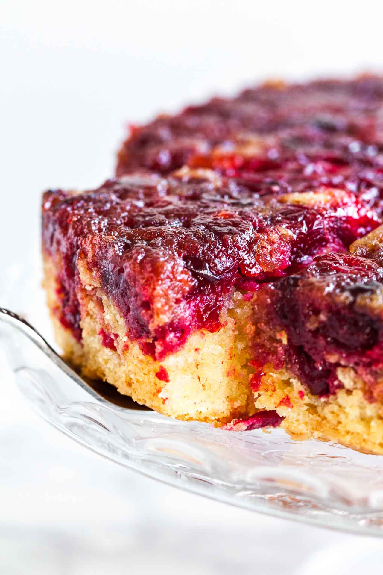 Un gâteau renversé aux canneberges sur un plateau de service en verre. Un serveur de gâteau soulève une tranche.