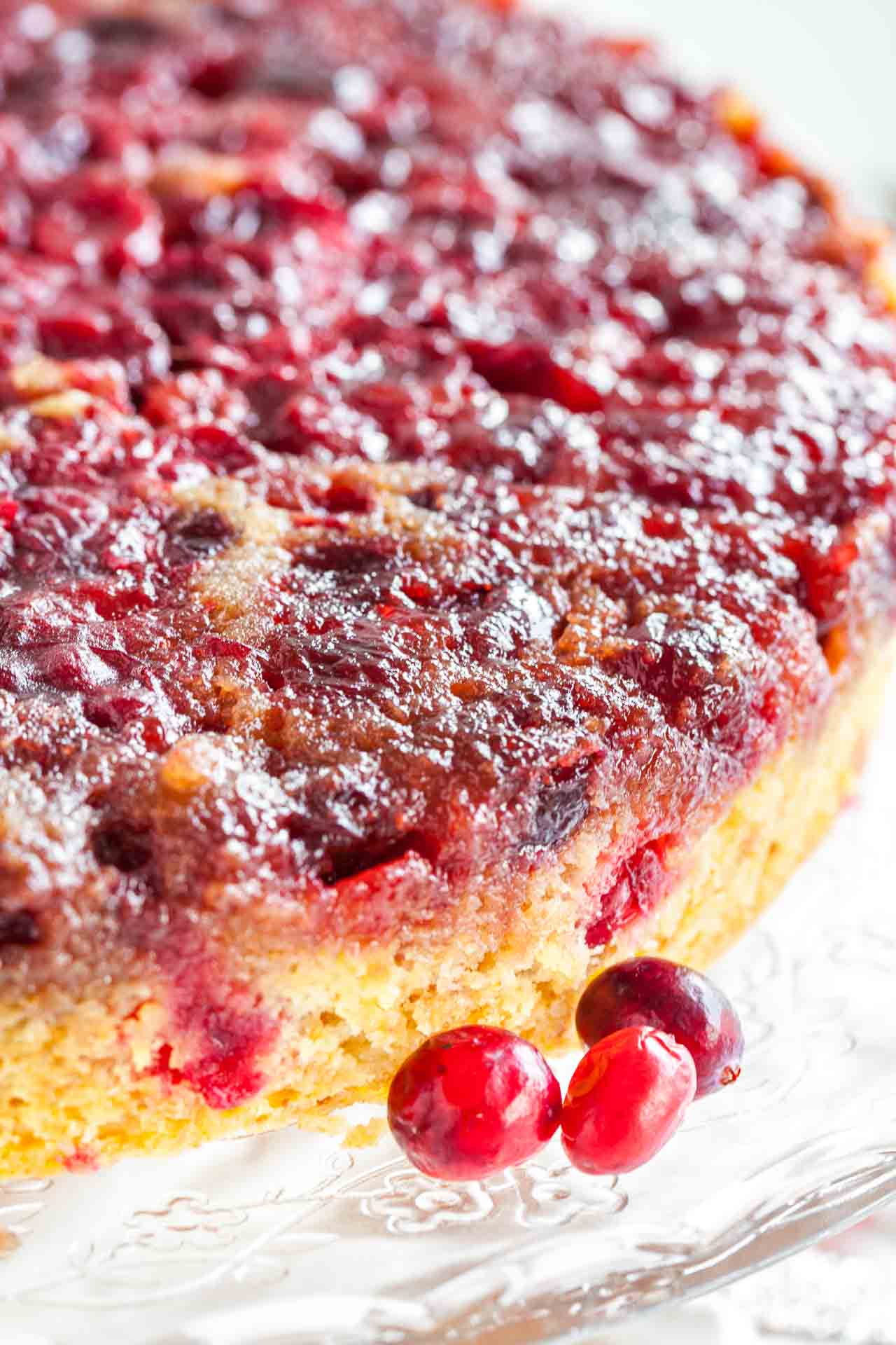Gros plan d'un gâteau renversé aux canneberges sur un plateau de service en verre, garni de canneberges.