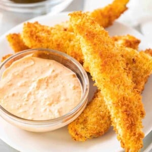 Une pile de cornichons à l'aneth frits à la friteuse à air sur une assiette blanche avec un petit bol avec une sauce.
