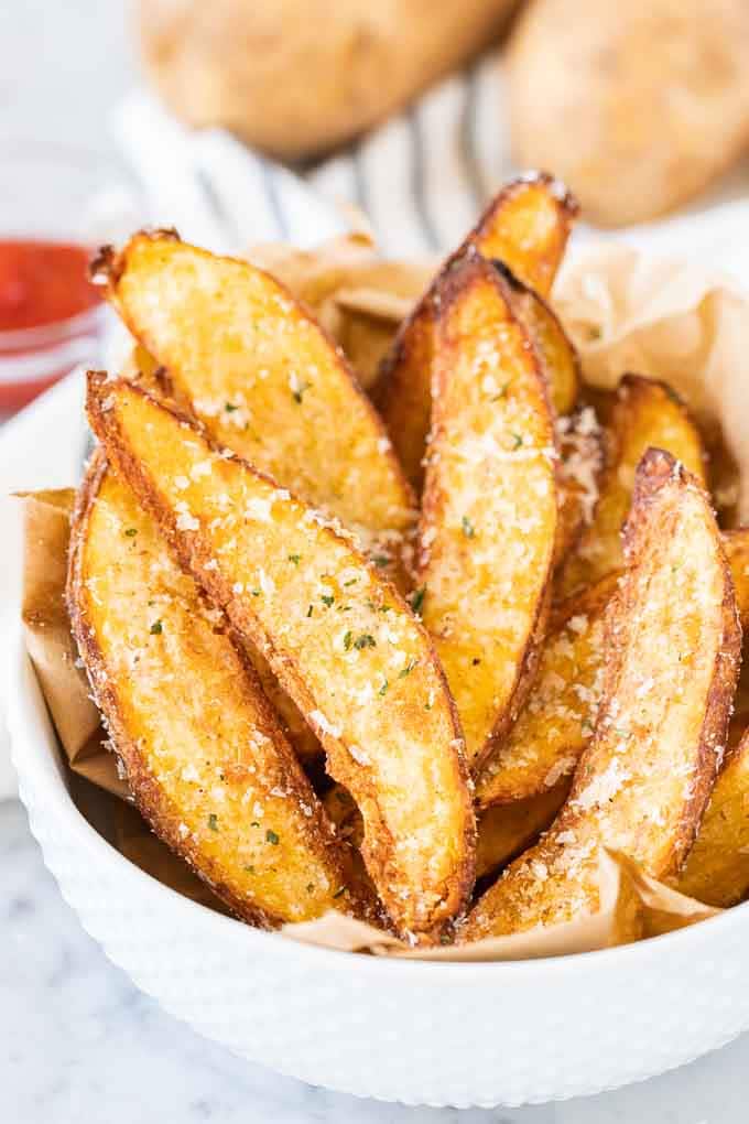Quartiers de pommes de terre dans un bol blanc, garnis de fromage parmesan.