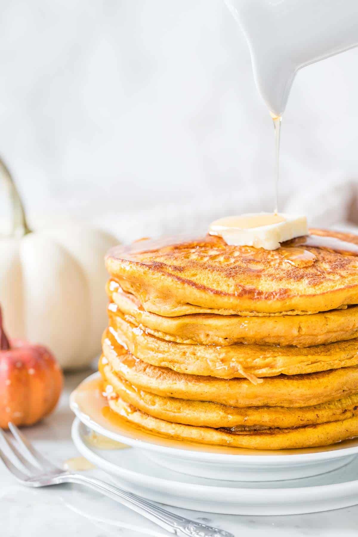 Une pile de crêpes à la citrouille garnies de beurre et de sirop d'érable.
