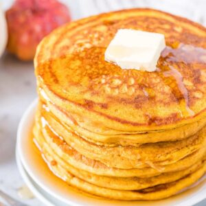 Une pile de crêpes à la citrouille garnies de beurre et de sirop d'érable.