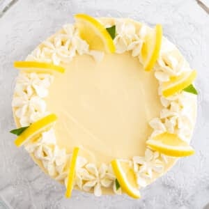 Vue de haut d'une tarte à la crème au citron garnie de crème fouettée et de tranches de citron sur un plat en verre sur une surface en marbre.