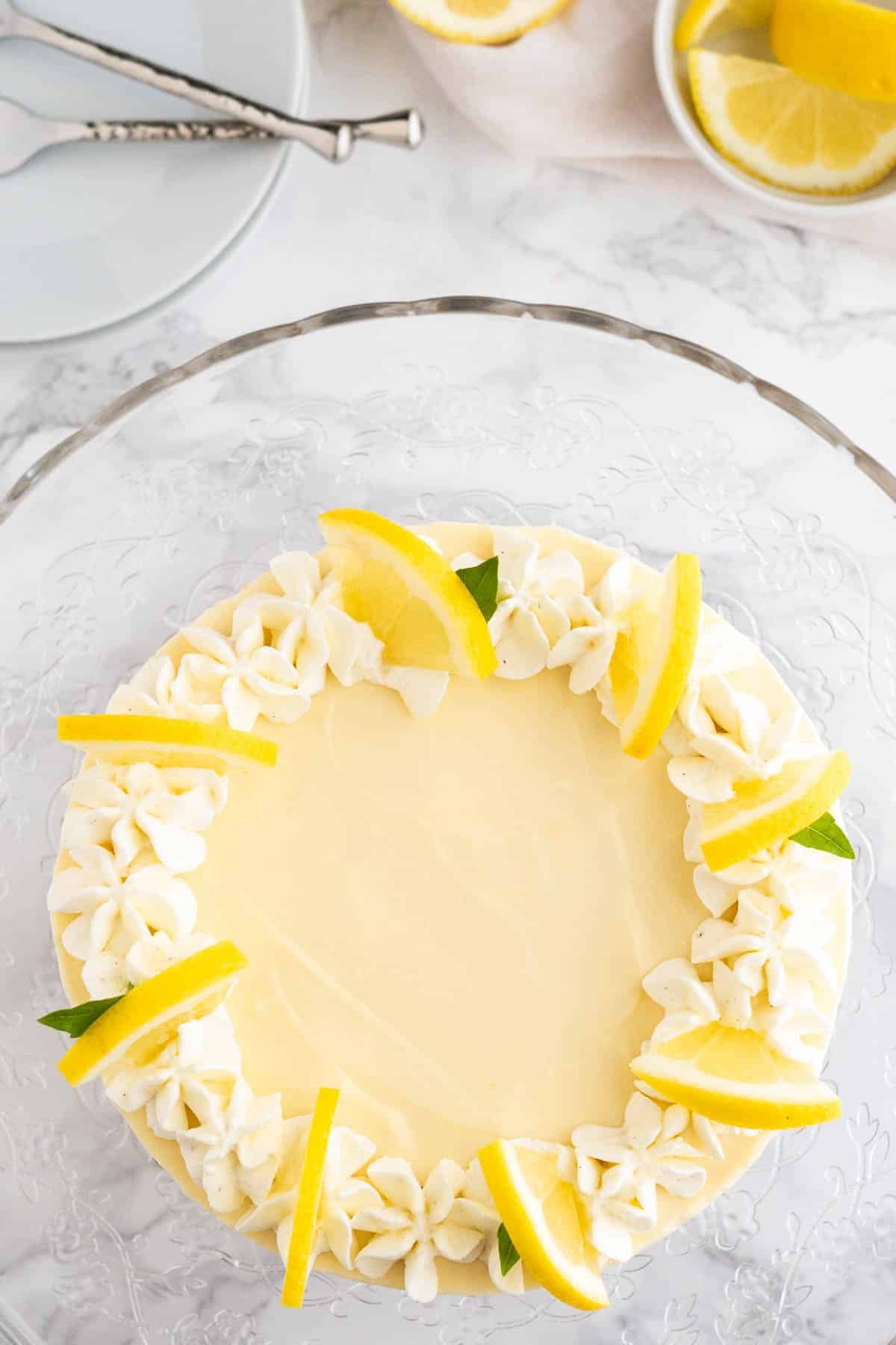 Vue de haut d'une tarte à la crème au citron garnie de crème fouettée et de tranches de citron sur un plat en verre sur une surface en marbre.
