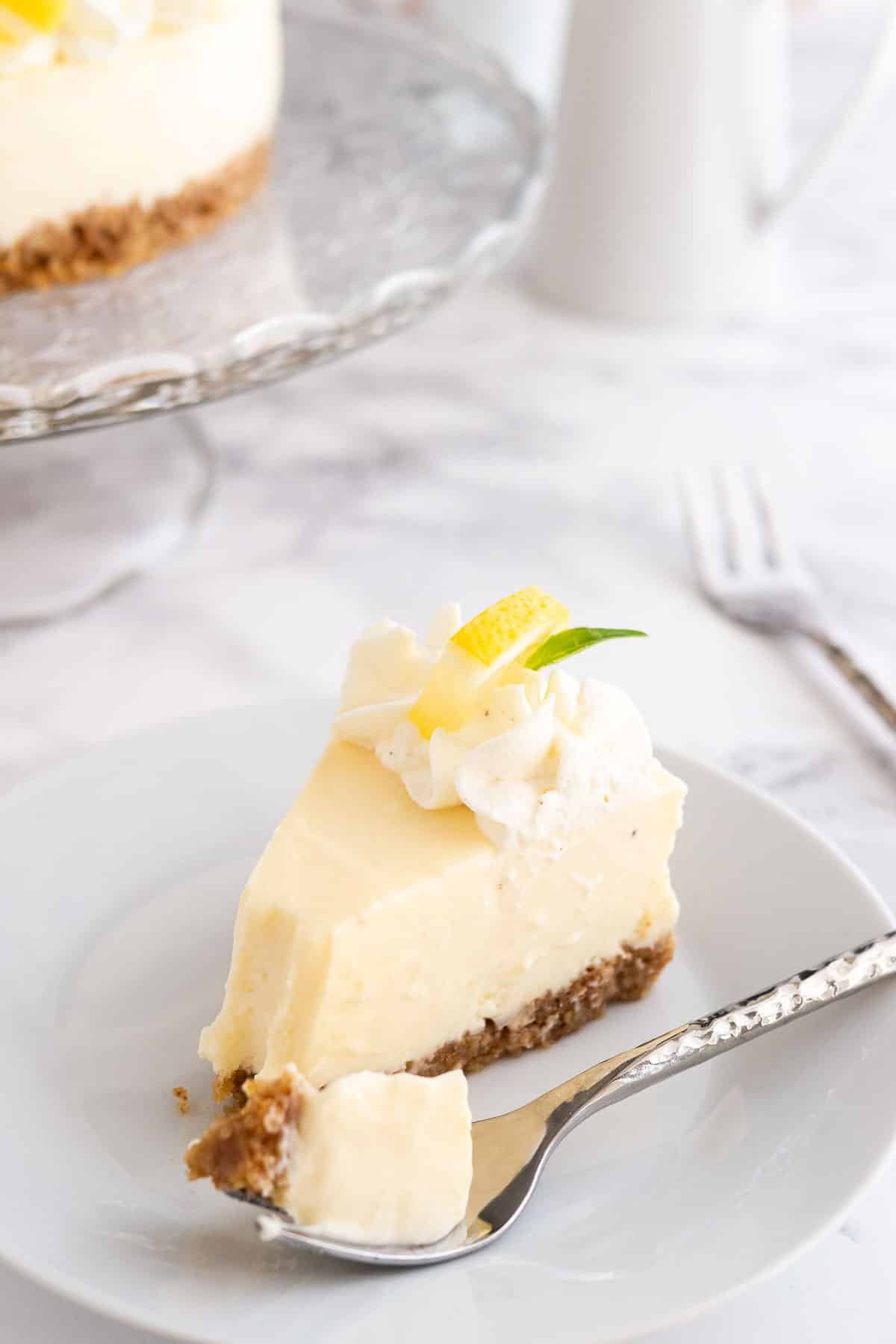 Une part de tarte à la crème au citron sur une assiette blanche avec une fourchette sur une surface en marbre.