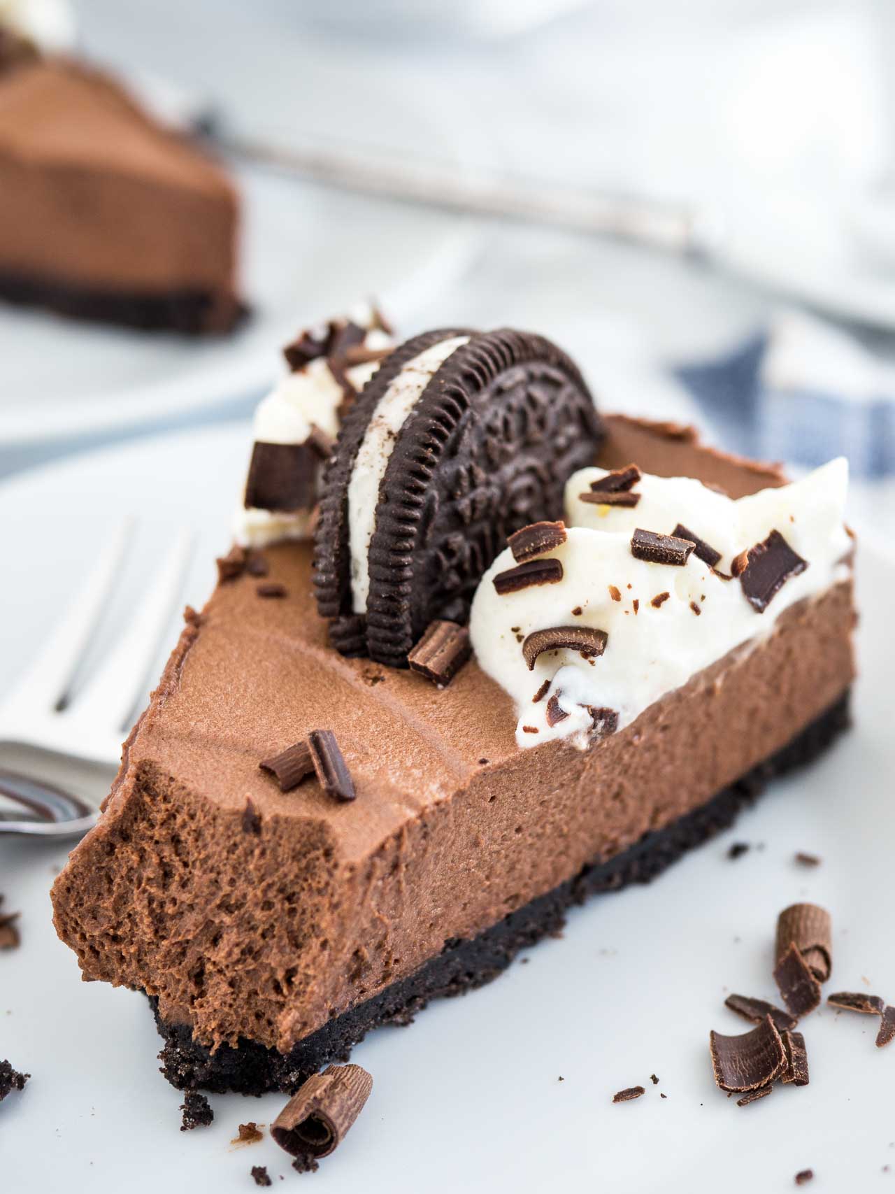 Ce gâteau au chocolat mousse est le rêve de tout amateur de chocolat et peut être préparé à l'avance ! Une croûte en Oreo remplie d'une mousse au chocolat décadente surmontée de plus d'Oreos, de crème fouettée faite maison et de copeaux de chocolat. Ce dessert sans cuisson est parfait pour des occasions spéciales mais si facile à préparer à partir de zéro ! #dessertsanscuisson #gâteauauchocolatmousse #mousseauchocolat #chocolat #recettes #desserts #gâteau Une tranche de gâteau au chocolat mousse sur une surface en marbre avec une fourchette à côté.