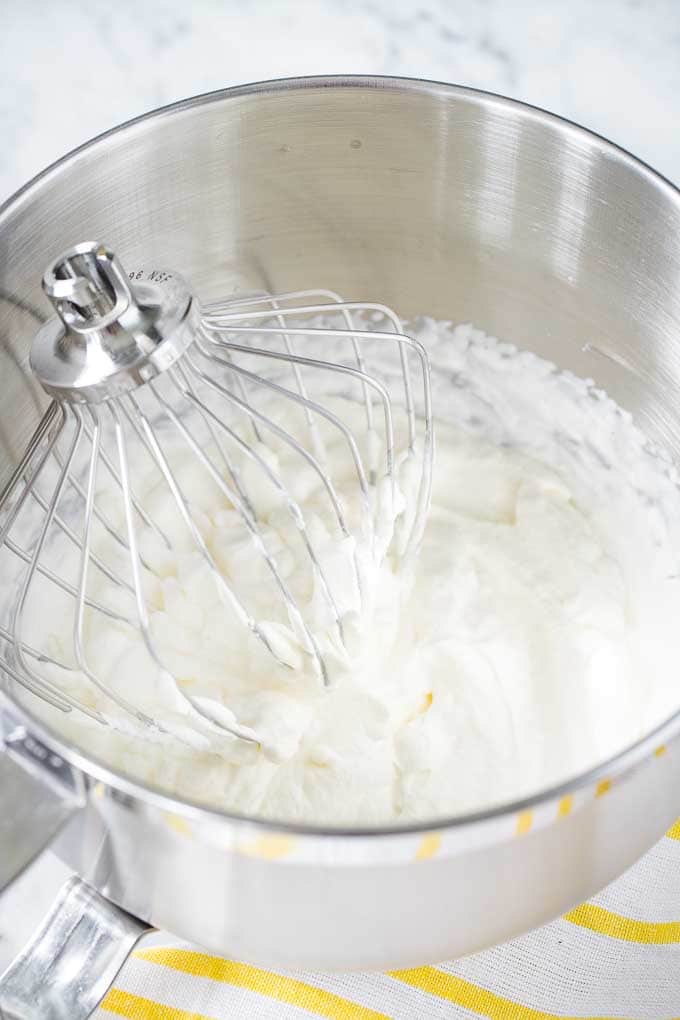 Crème chantilly dans un bol en acier inoxydable, avec un fouet Kitchen Aid.