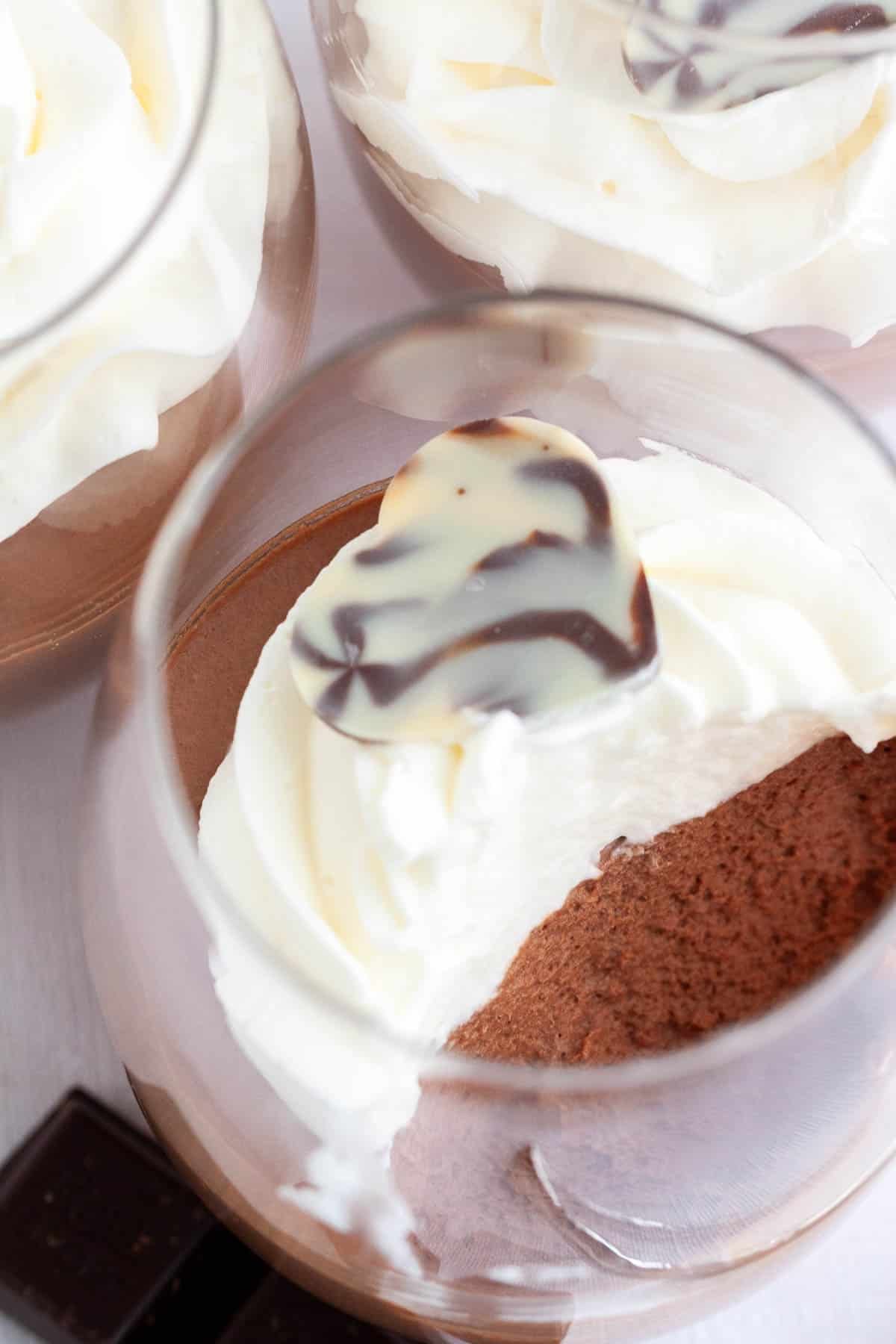 Cette recette de mousse au chocolat est super simple à réaliser maison et délicieusement légère et aérée. Une recette de mousse sans œuf qui est si aérienne et chocolatée et peut être appréciée par tout le monde. Assez élégante pour une fête, mais suffisamment facile à préparer chaque fois que vous avez une envie de chocolat ! Vue de dessus de 3 verres de mousse au chocolat surmontés de crème fouettée.