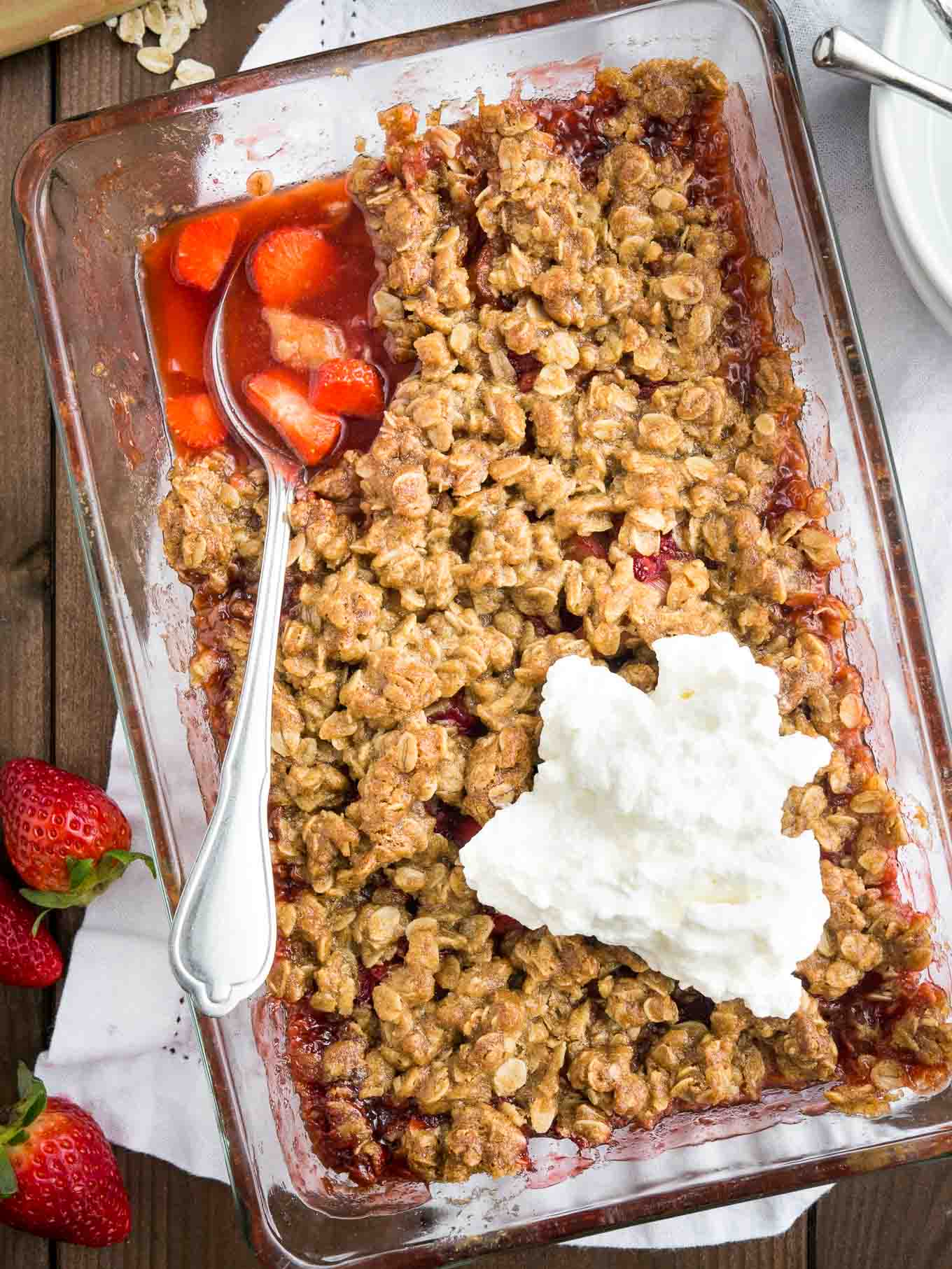 Crumble aux fraises et à la rhubarbe dans un plat en verre sur une table en bois.
