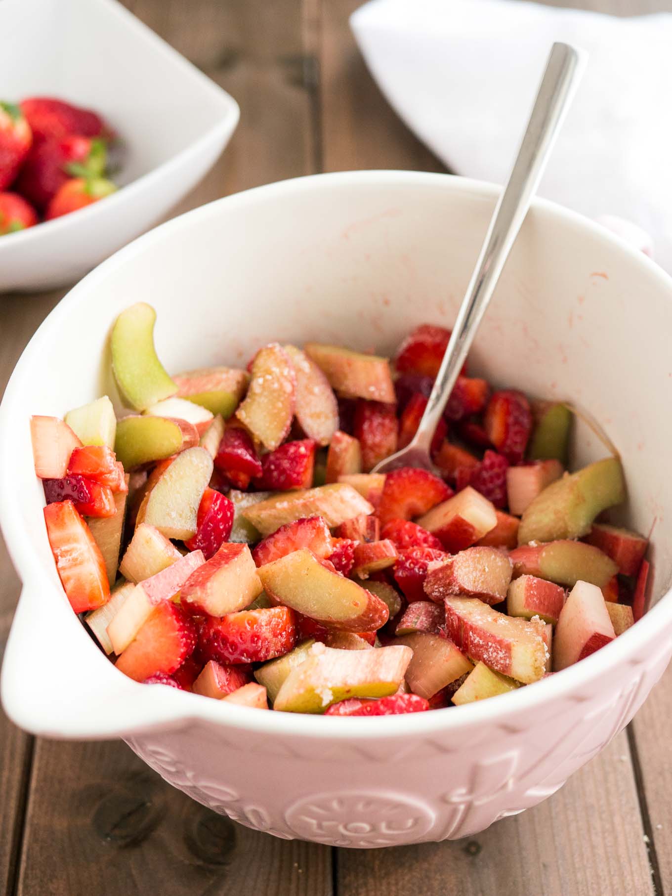 Fraises et rhubarbe tranchées dans un bol rose avec une fourchette, des fraises fraîches dans un bol en arrière-plan.