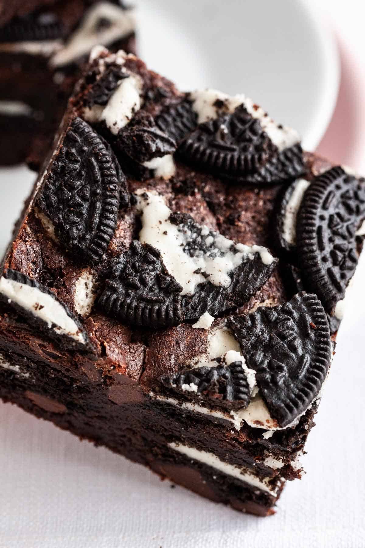 Un brownie avec des Oreos sur le dessus, penché contre une assiette.