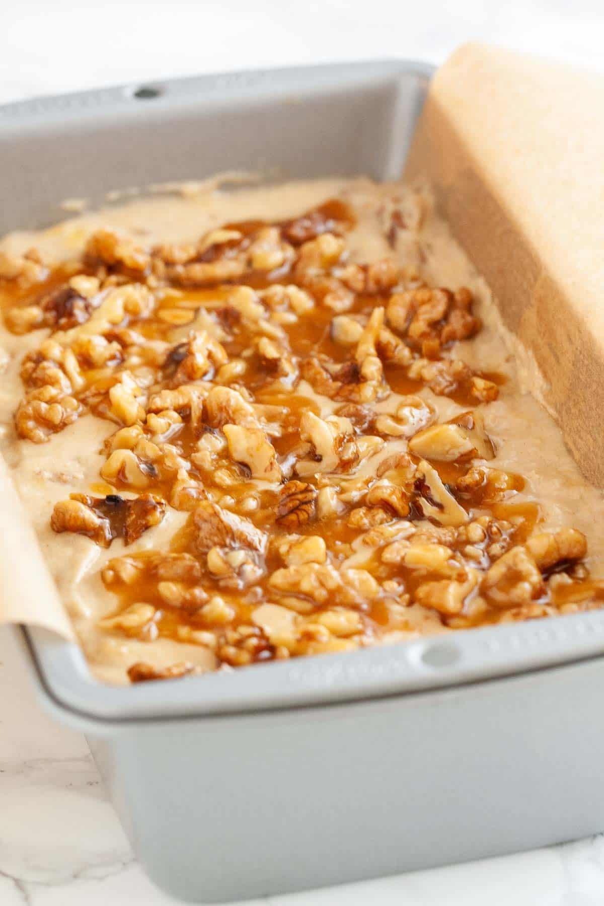 Ce pain à la banane est très moelleux et délicieux ! Surmonté de noix caramélisées et chargé de noix et de bananes écrasées, ma recette de pain à la banane est un favori de la famille qui est parfait pour le petit-déjeuner ou comme collation. Une façon idéale d'utiliser des bananes trop mûres ! #painbanane #painbananeauxnoix #recettesbananes #bananes #pain #recettespetitdéjeuner Un moule à pain, tapissé de papier sulfurisé, rempli de pâte à pain à la banane et aux noix.