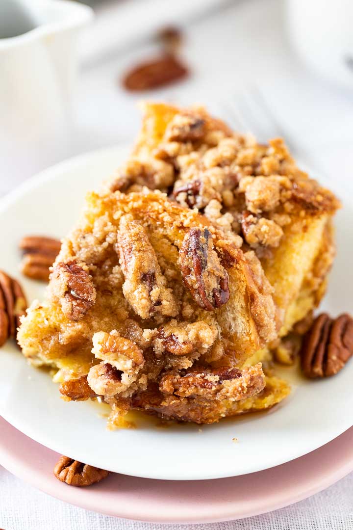 Gros plan d'un morceau de casserole de pain perdu sur une assiette blanche garnie de noix de pécan.