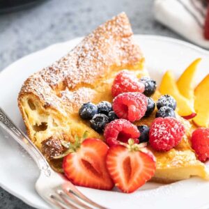 Une part de pancake néerlandais sur une assiette blanche garnie de fruits.