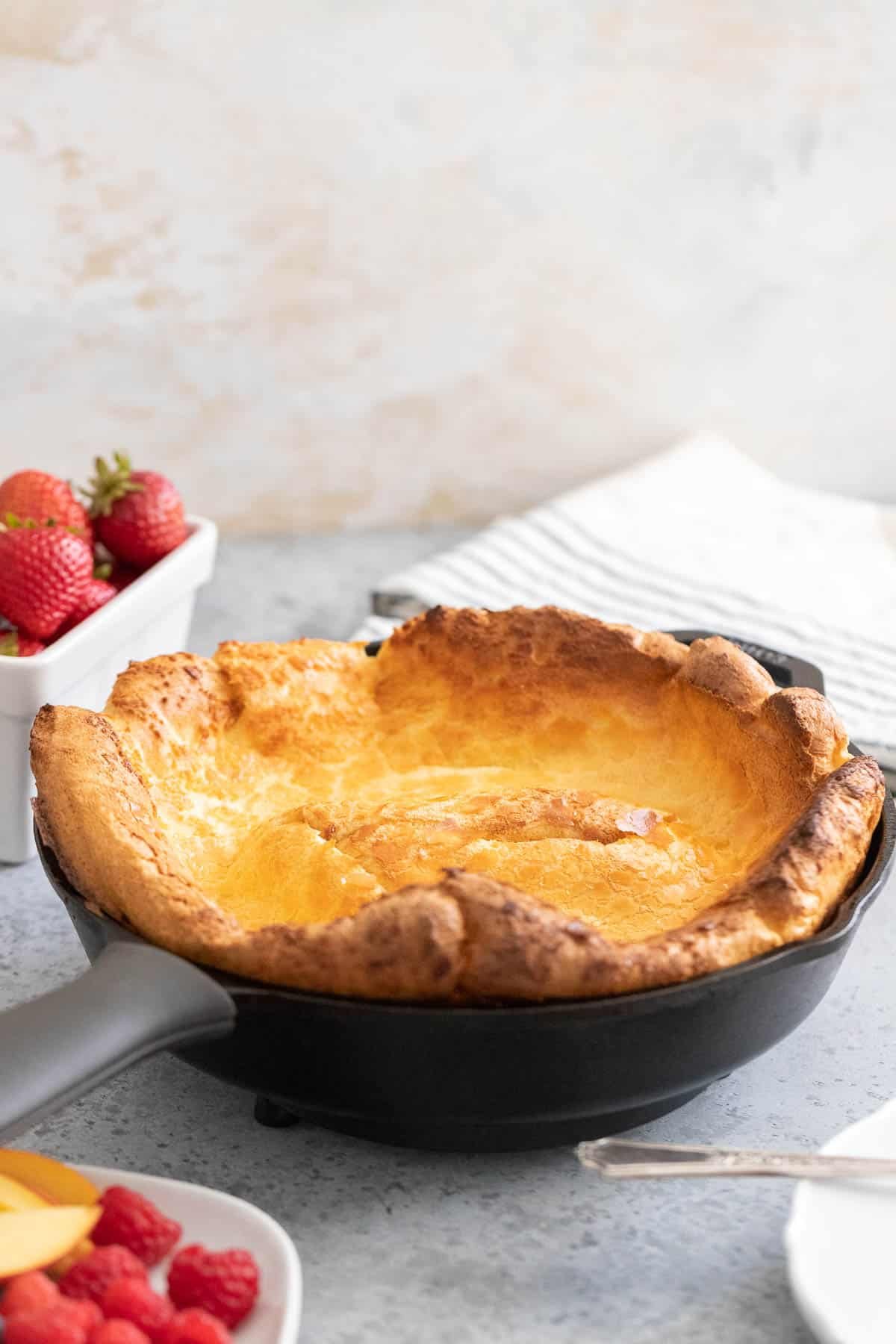 Un pancake néerlandais dans une poêle en fonte à côté d'un bol de fraises.