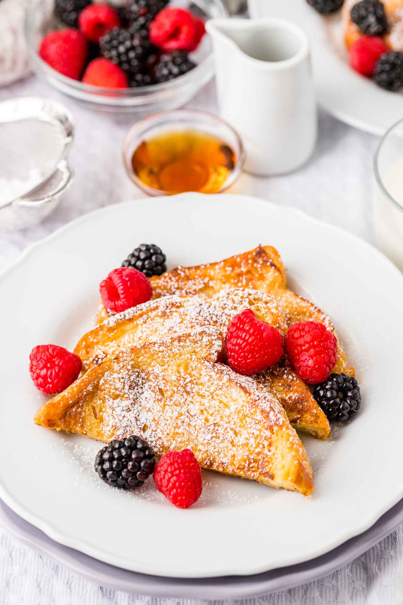 Pain perdu garni de sucre glace et de baies sur une assiette blanche.