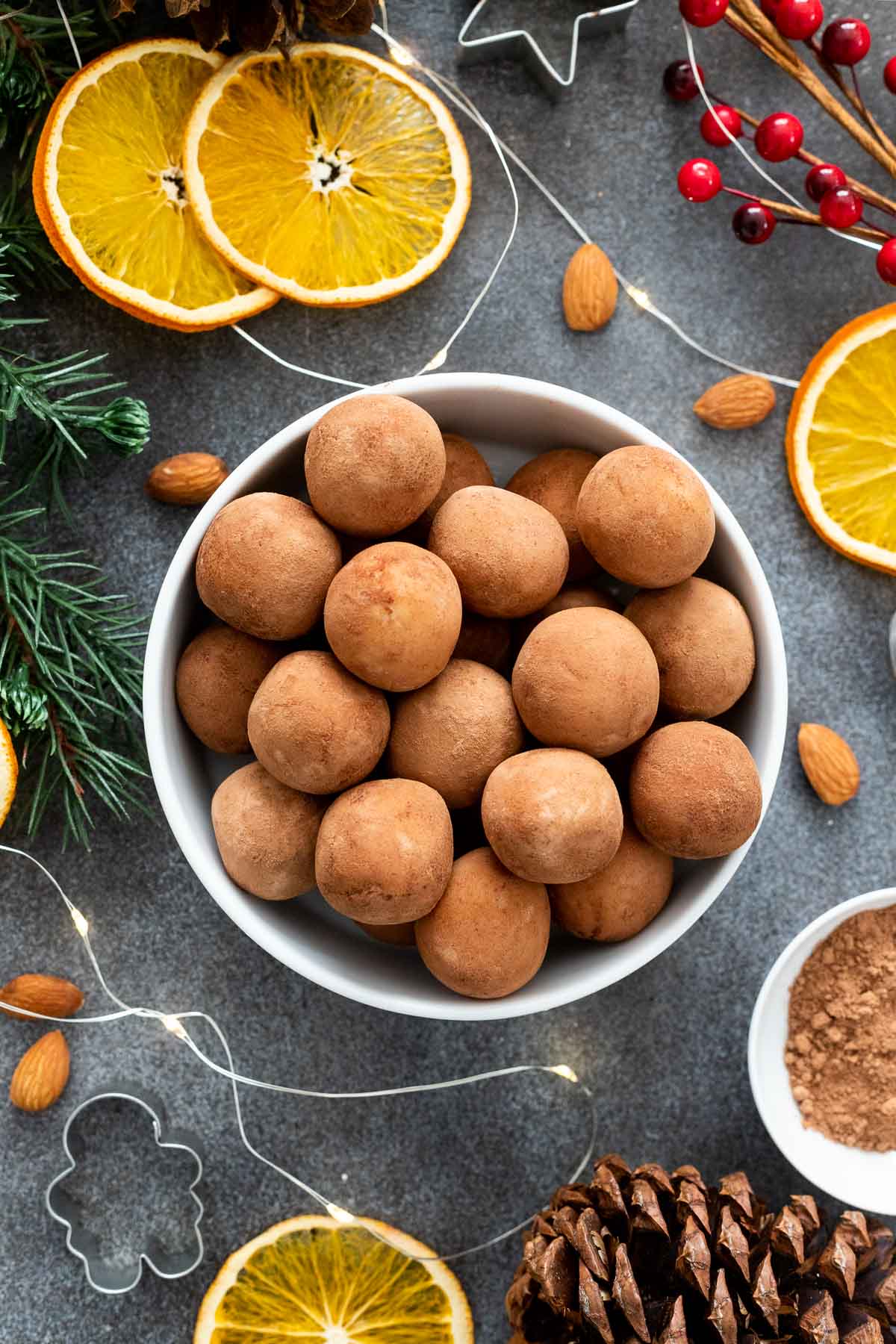Marzipankartoffeln dans un bol blanc sur une planche noire, à côté se trouvent des tranches d'orange et des amandes.