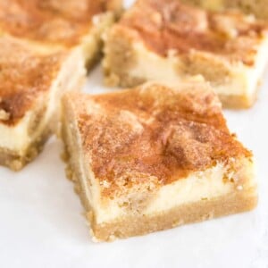 Des barres de cheesecake snickerdoodle sur du papier parchemin. La plus proche est tournée à 45 degrés.