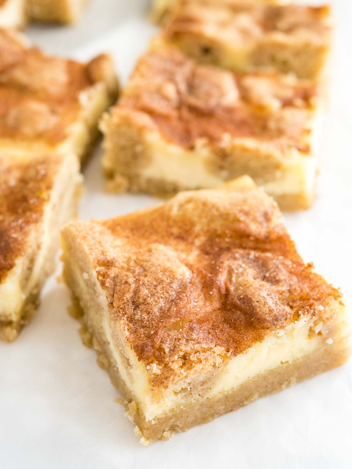 Gros plan sur des barres de cheesecake snickerdoodle sur du papier parchemin. La plus proche est tournée à 45 degrés.