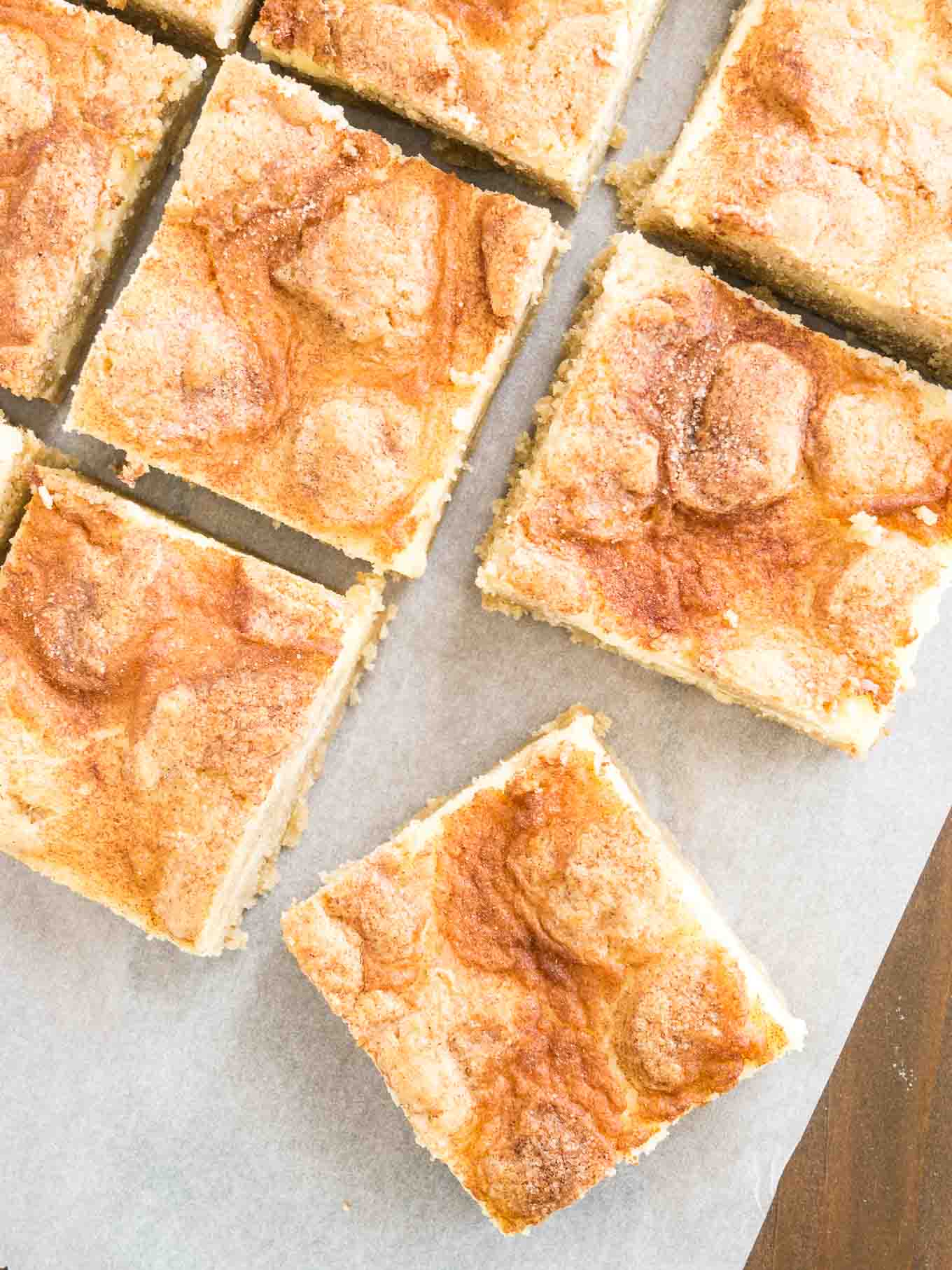 Vue de dessus sur des barres de cheesecake snickerdoodle sur du papier parchemin. La plus proche est tournée à 45 degrés.