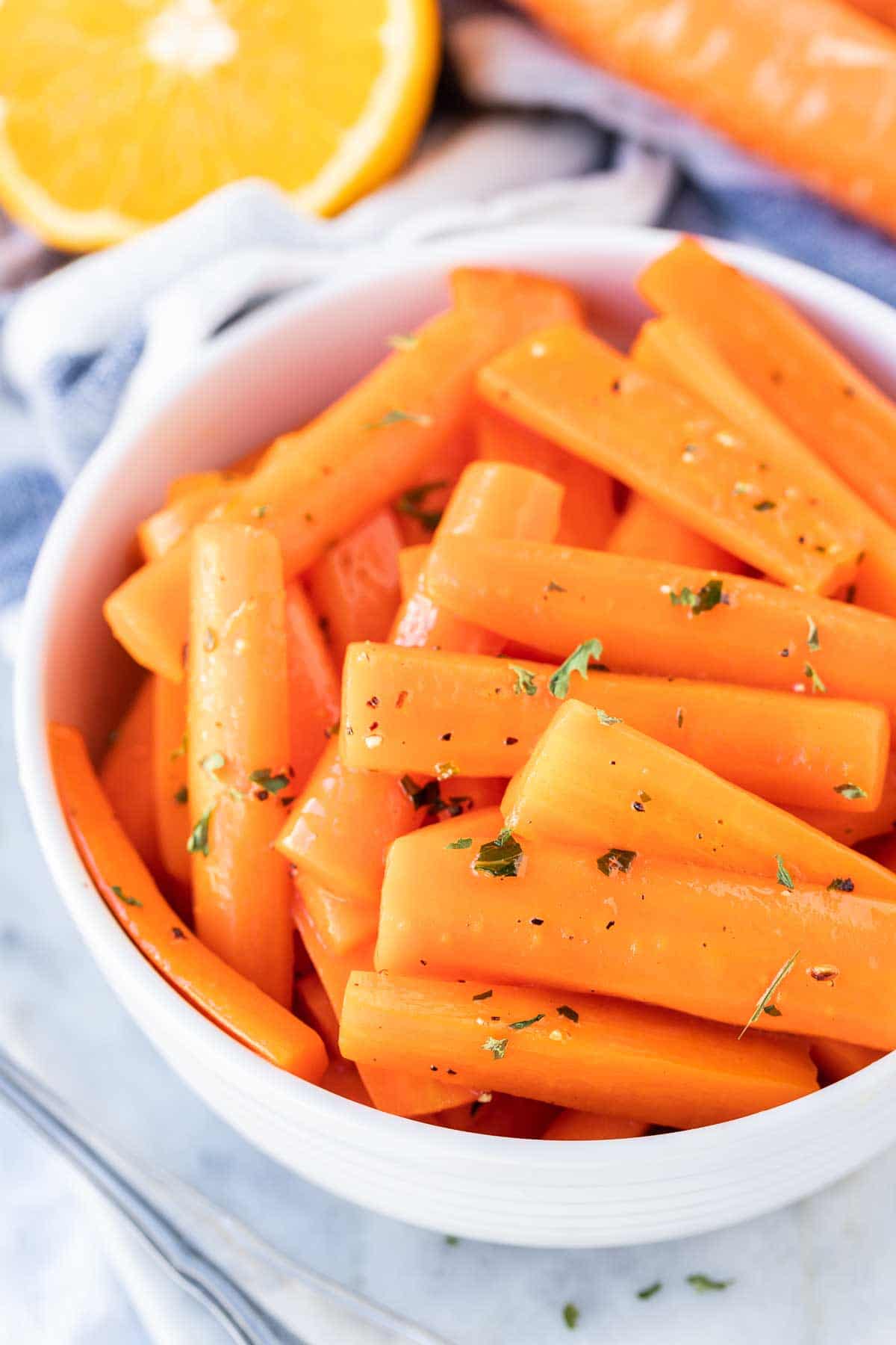 Carottes glacées dans un plat de service avec une orange à côté.