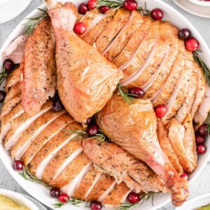 Une dinde entière tranchée sur un plat de service blanc garnie de canneberges et de romarin