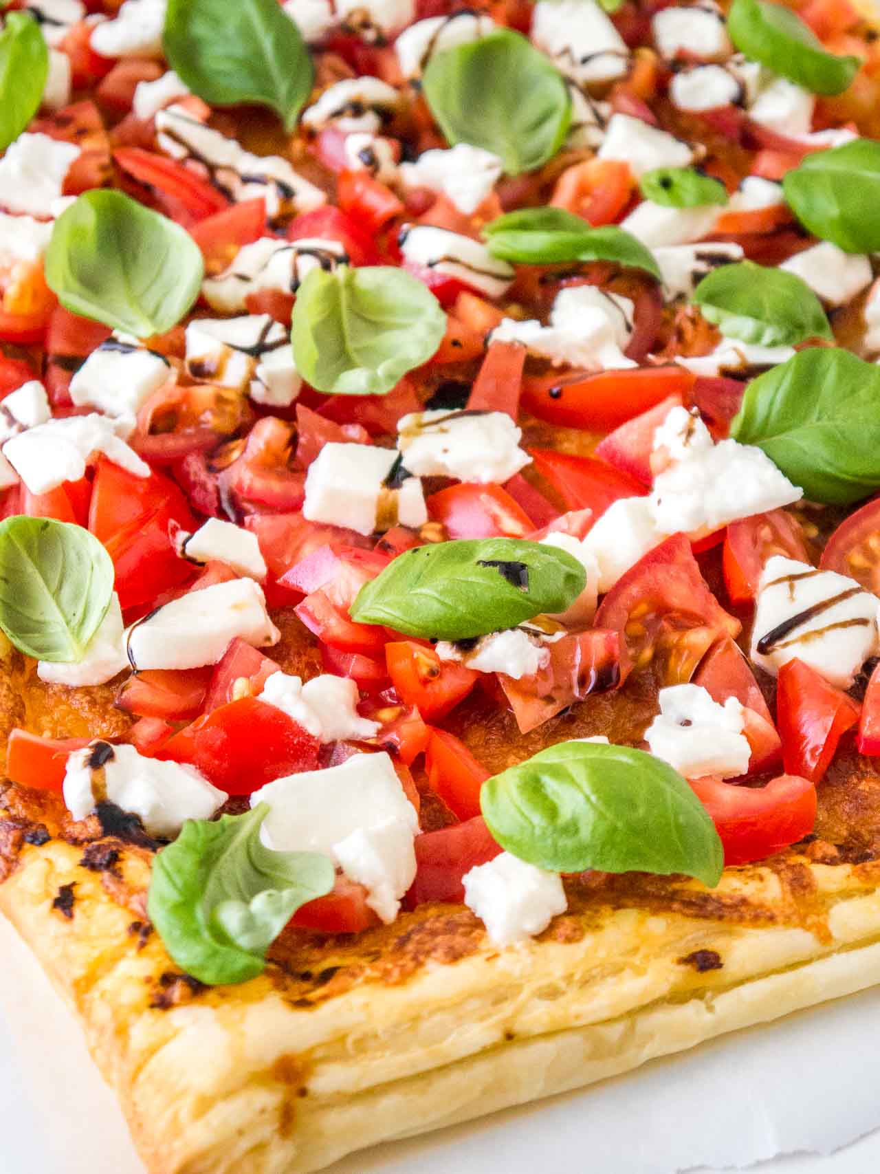 Gros plan de pizza en pâte feuilletée tomate mozzarella avec tomates, mozzarella, feuilles de basilic et glaçage balsamique.