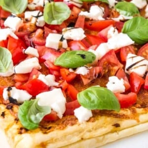 Gros plan de pizza en pâte feuilletée tomate mozzarella avec tomates, mozzarella, feuilles de basilic et glaçage balsamique.