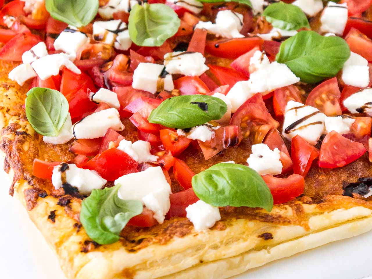 Gros plan de pizza en pâte feuilletée tomate mozzarella avec tomates, mozzarella, feuilles de basilic et glaçage balsamique.