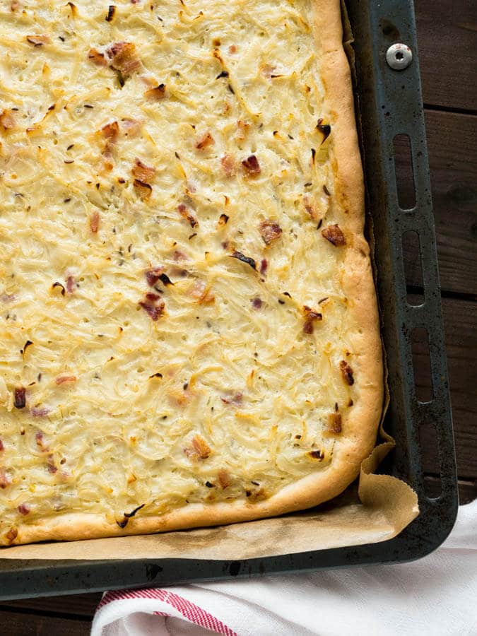 Vue de haut d'une plaque de cuisson tapissée de papier sulfurisé avec de la tarte à l'oignon sur une table en bois.