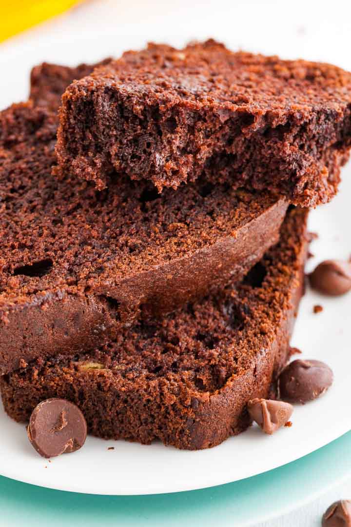 Deux tranches et demie de pain à la banane et au chocolat empilées sur une assiette blanche, garnies de quelques pépites de chocolat. La tranche du dessus a été coupée en deux.