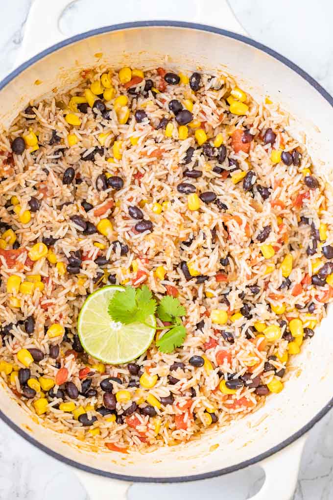 Riz et haricots dans une poêle blanche, garnis d'une tranche de citron vert et de coriandre.
