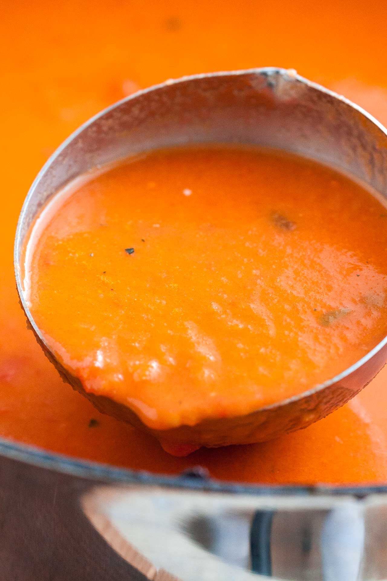 Gros plan d'une louche puisant de la soupe de tomates d'un pot.