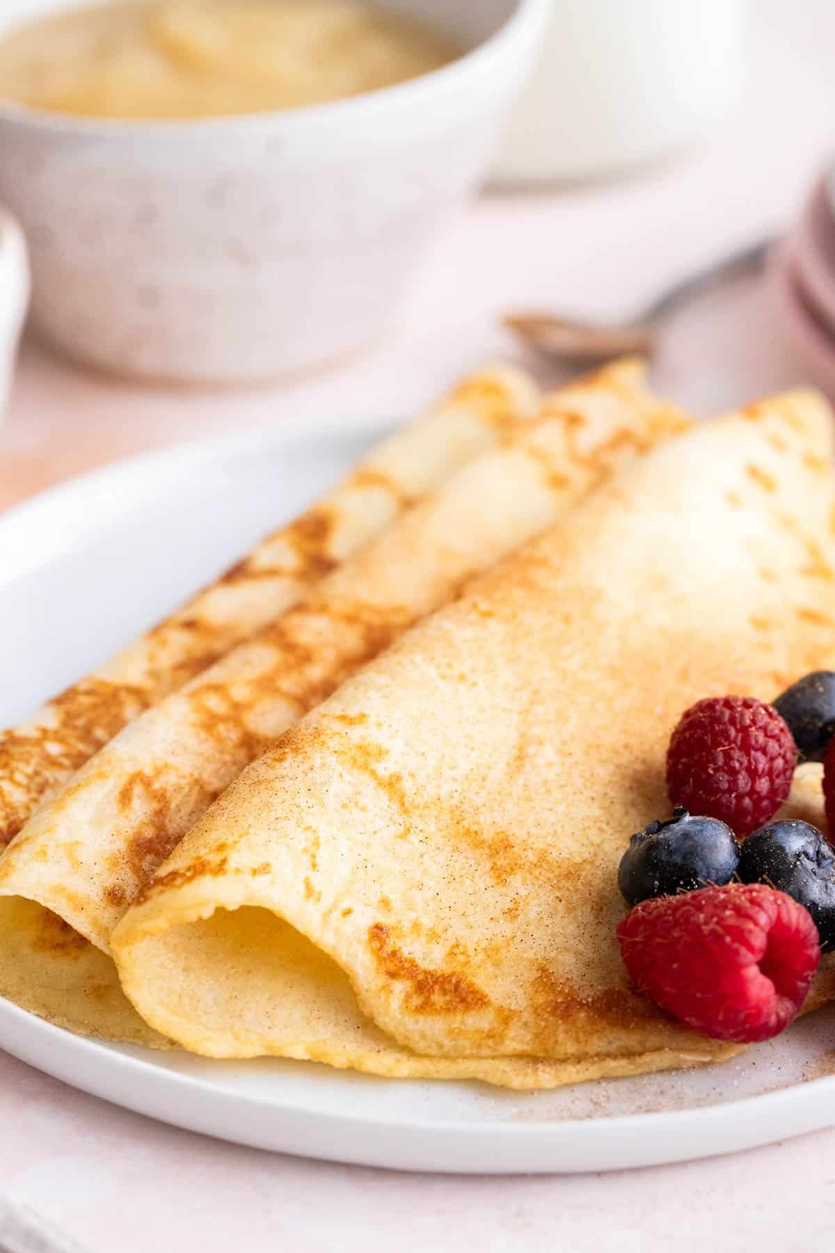 Trois crêpes à côté de baies sur une assiette.