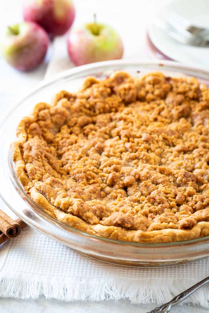 Un plat en verre, avec tarte aux pommes avec streusel garnie de pommes et de bâtons de cannelle