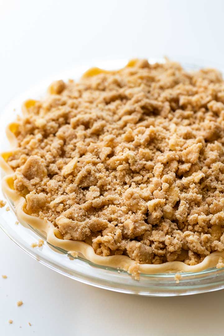 Gros plan d'un plat en verre avec la tarte aux pommes avec streusel avant cuisson. La croûte est ondulée tout autour.