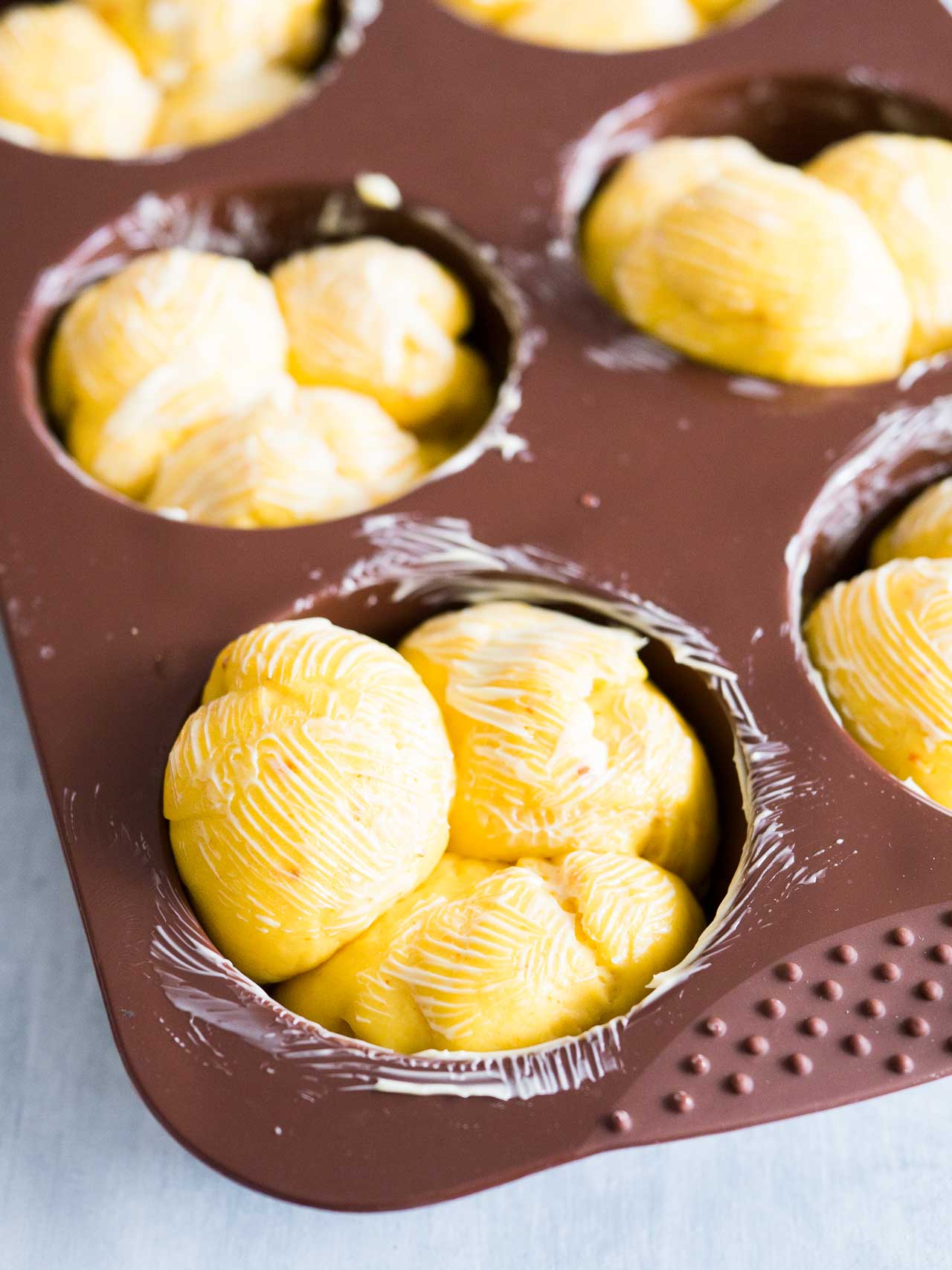 Un moule à muffins beurré avec 3 morceaux de pâte dans chaque cavité. Chaque morceau a du beurre sur le dessus.