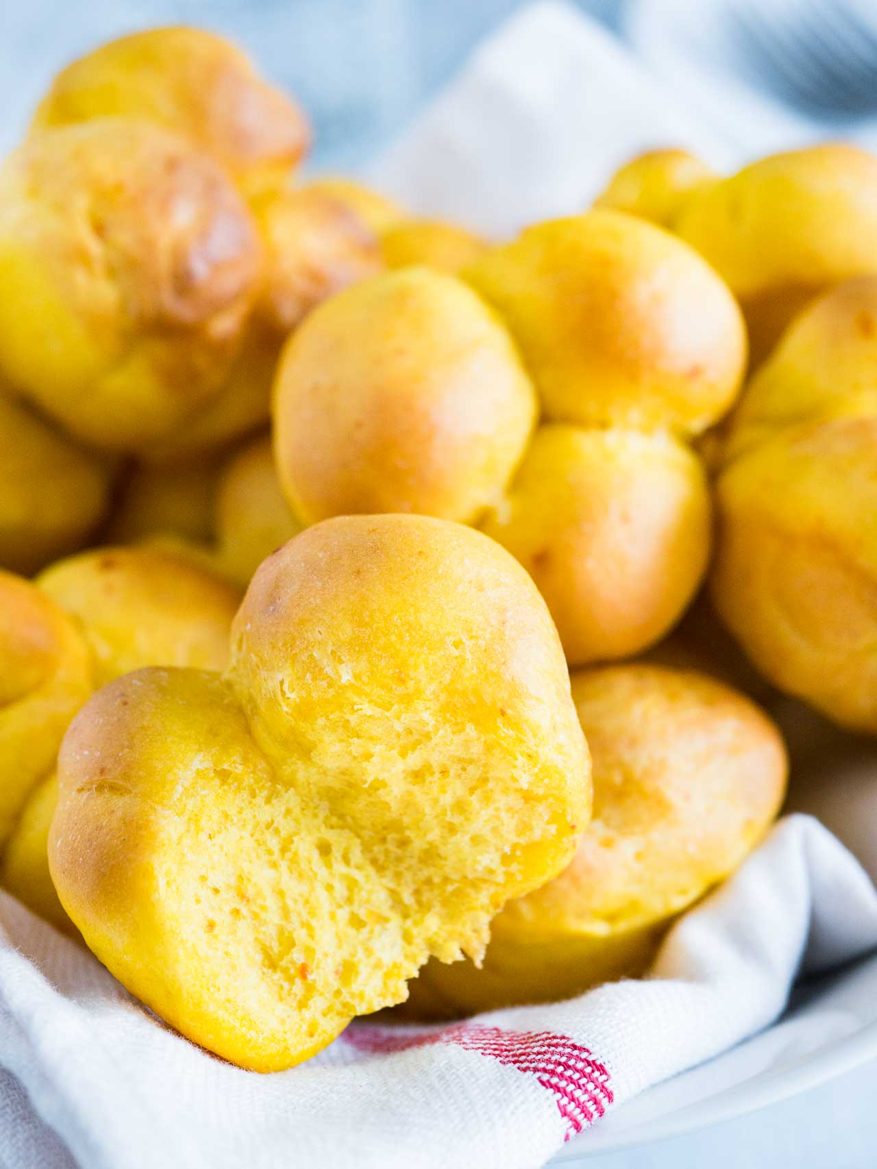 Petits pains à la citrouille sur un torchon blanc avec une bande rouge. L'un des petits pains a un morceau manquant.