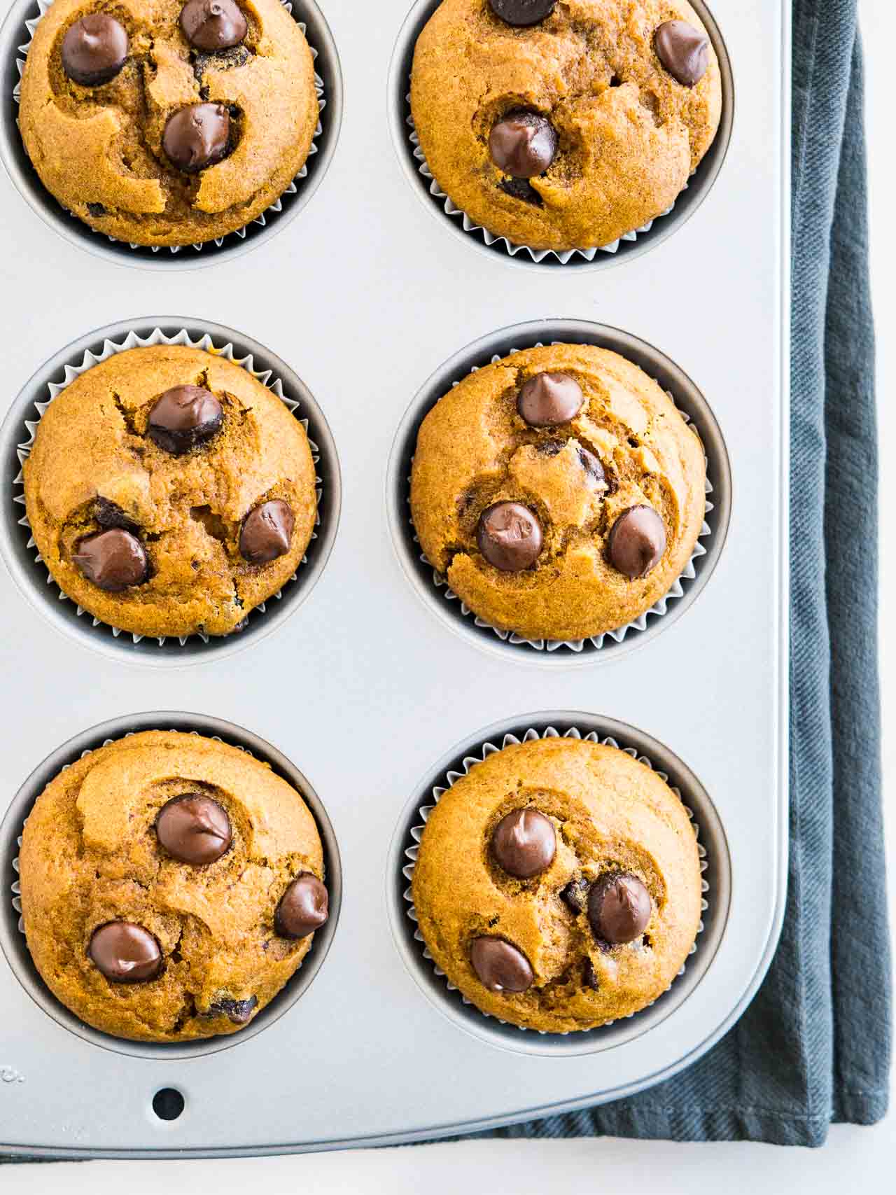 Vue de haut d'un moule à muffins gris avec des muffins à la citrouille et aux pépites de chocolat cuits sur un torchon gris.
