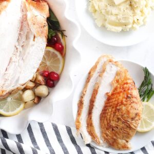 Poitrine de dinde tranchée sur une assiette à côté d'un bol de purée de pommes de terre et d'une poitrine de dinde entière