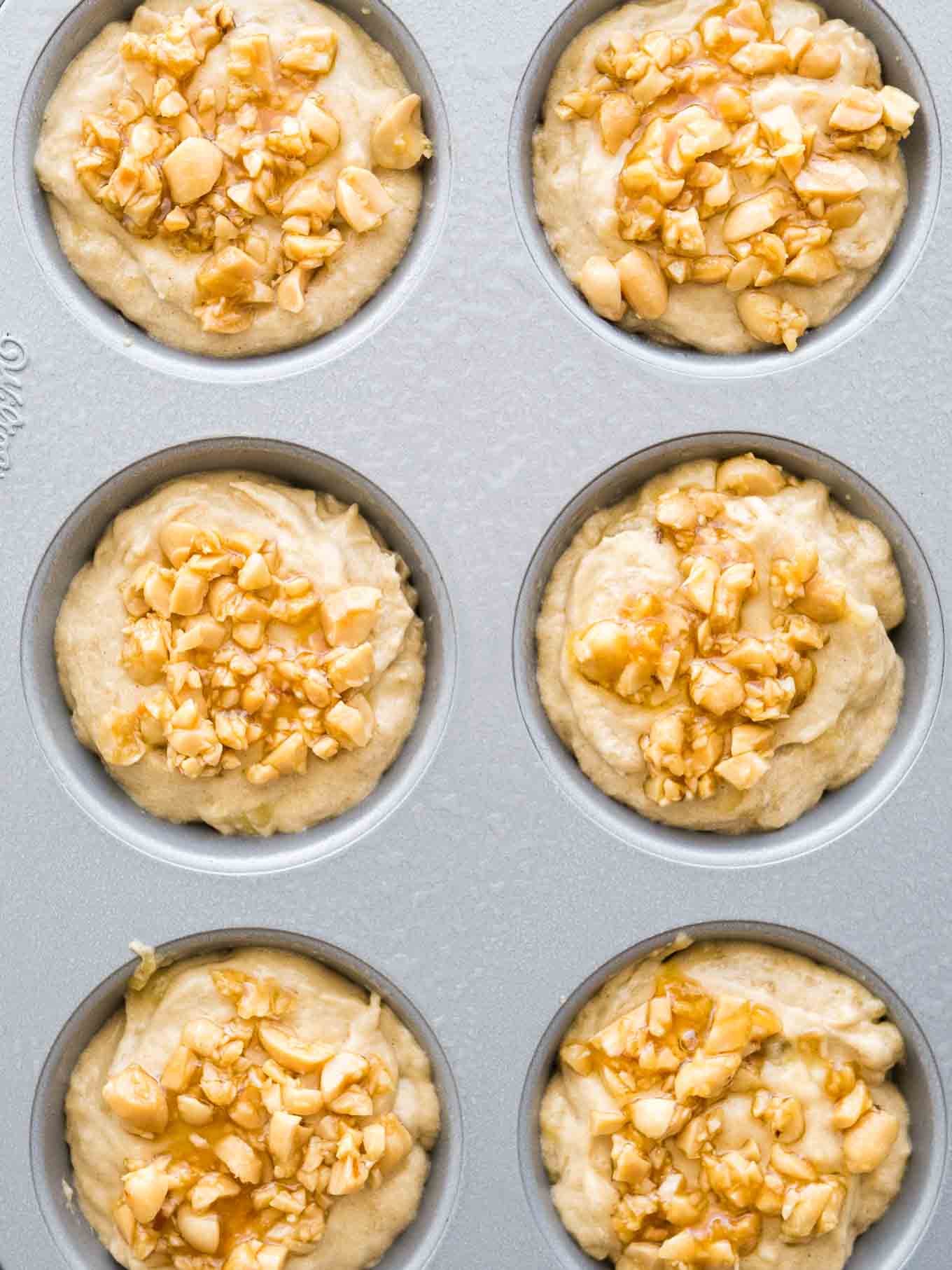 Vue par le haut d'un moule à muffins gris avec de la pâte à muffins garnie de cacahuètes avant cuisson.
