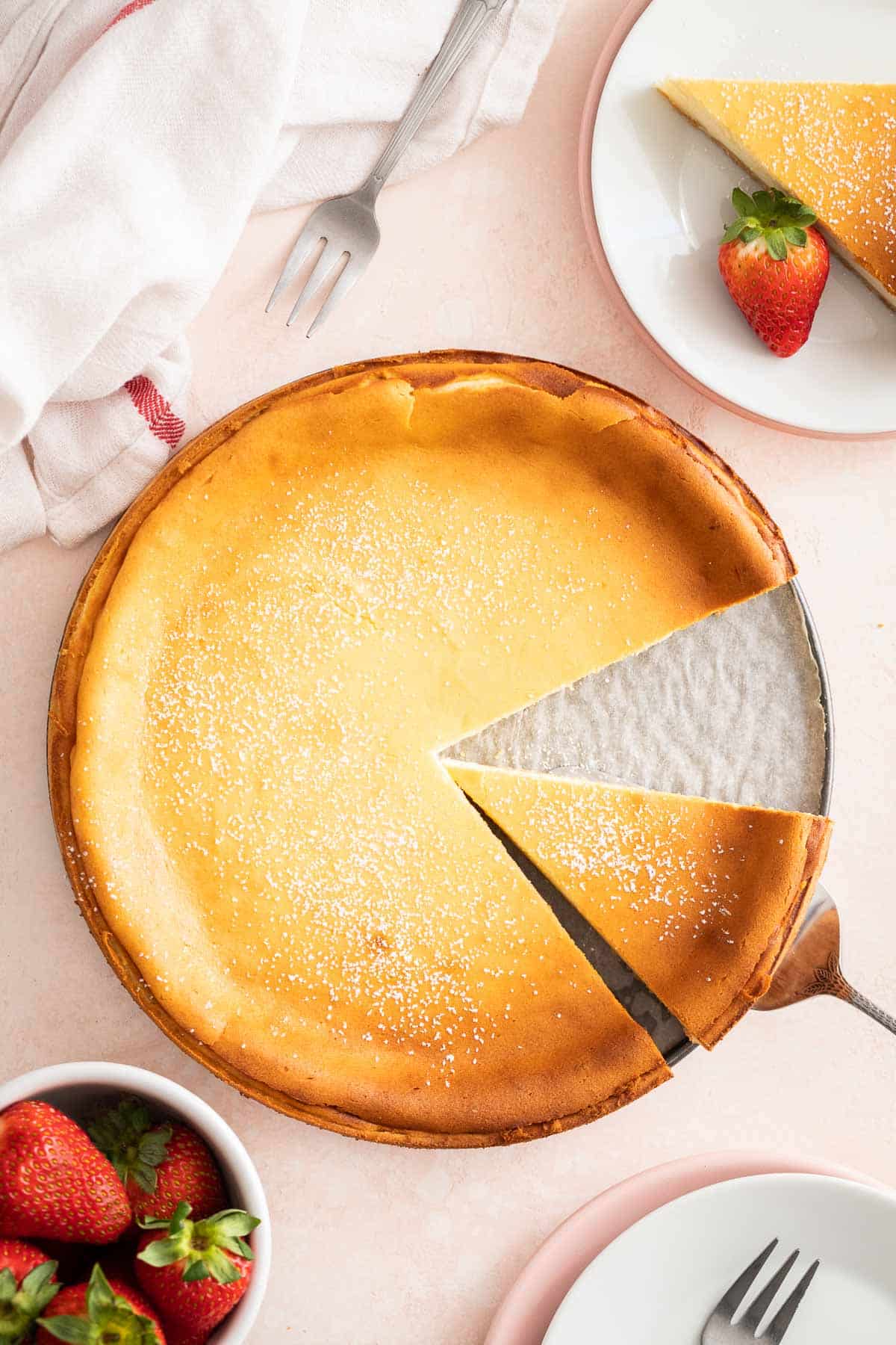 Un cheesecake allemand sur une surface rose clair à côté de fraises et d'assiettes.