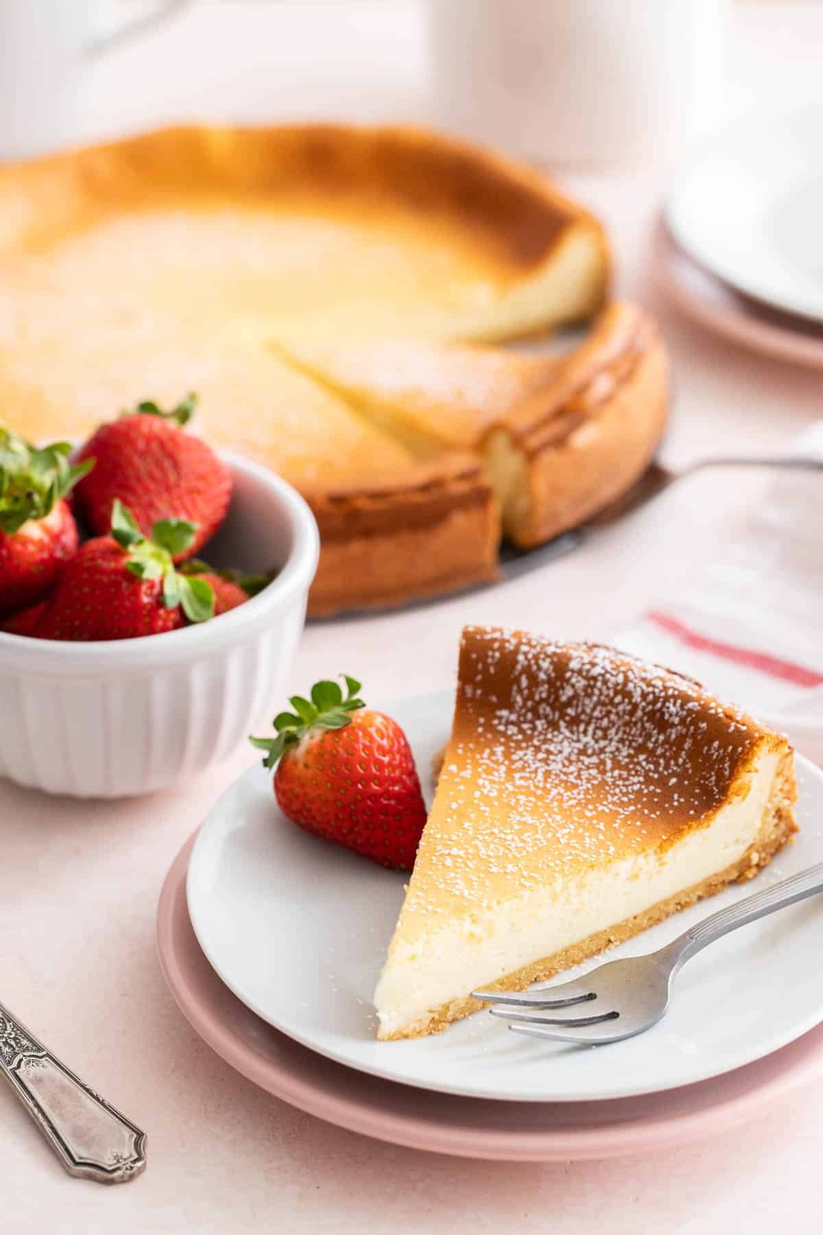 Un cheesecake sur un plat à gâteau avec une tranche de gâteau devant lui.