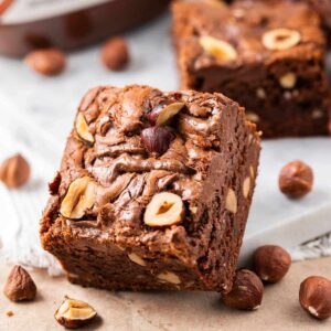 Brownie au Nutella s'appuyant contre une assiette blanche avec des noisettes, un pot de Nutella et plusieurs brownies au Nutella en arrière-plan
