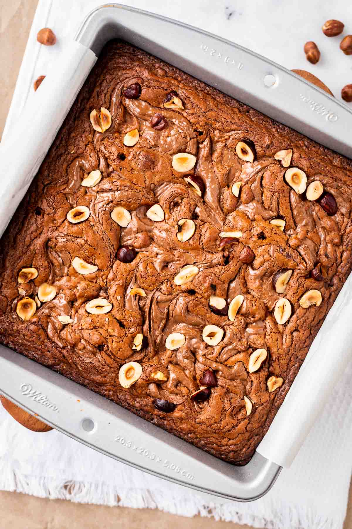Un moule à pâtisserie plein de brownies saupoudrés de noisettes.