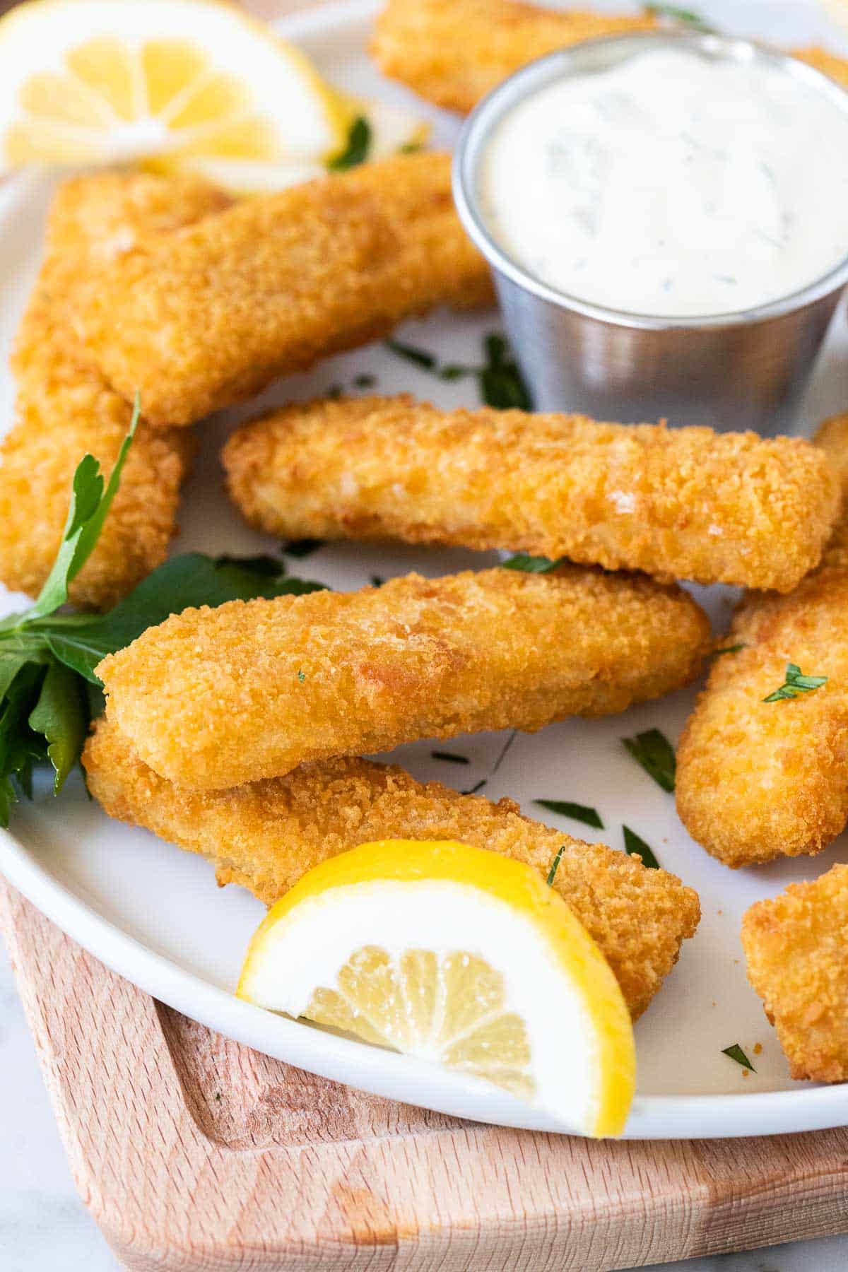 Une tranche de citron, des bâtonnets de poisson, et de la sauce tartare sur une assiette.