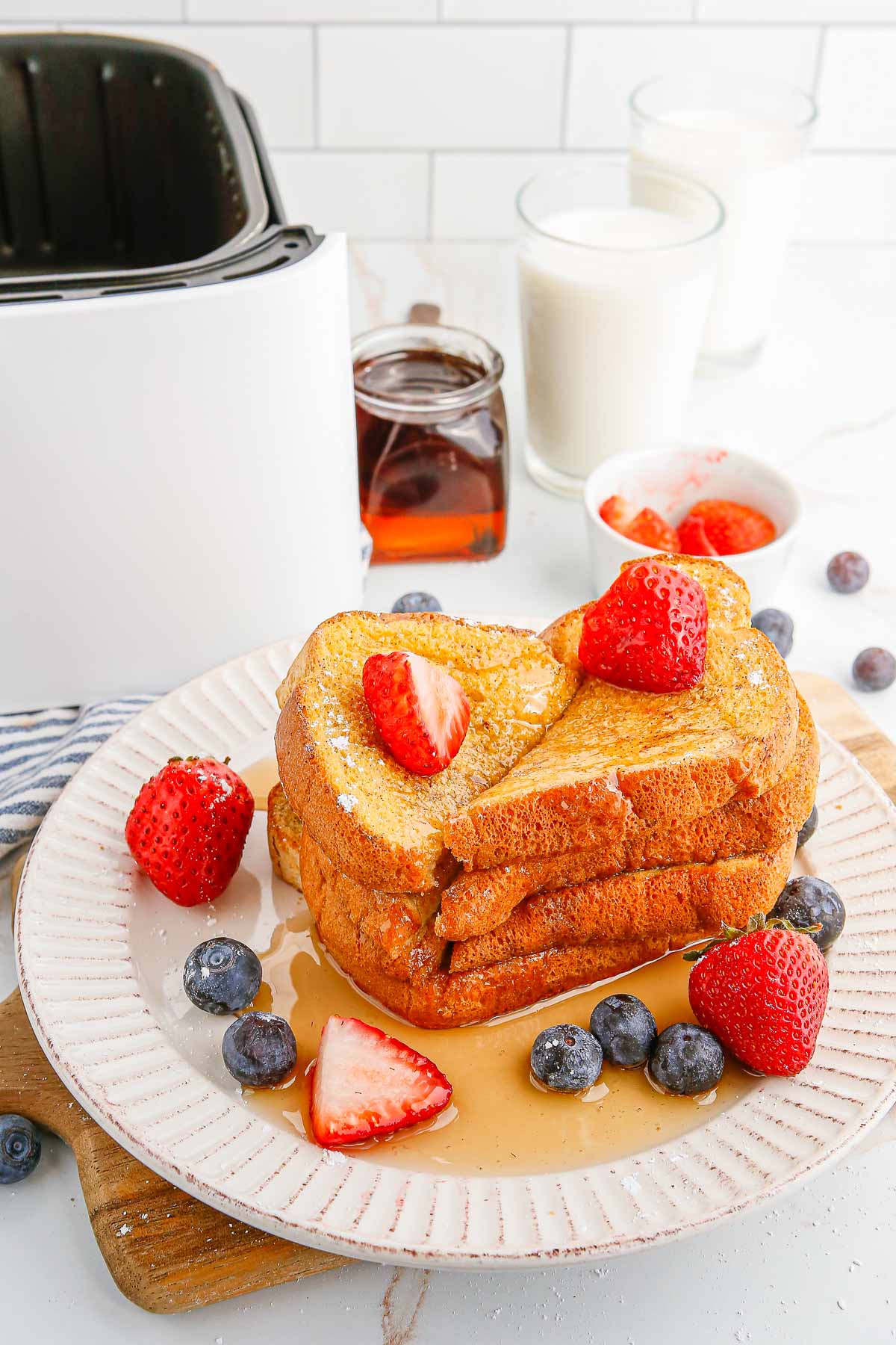 Une assiette de pain perdu garnie de fruits et de sirop à côté d'un panier de friteuse à air.
