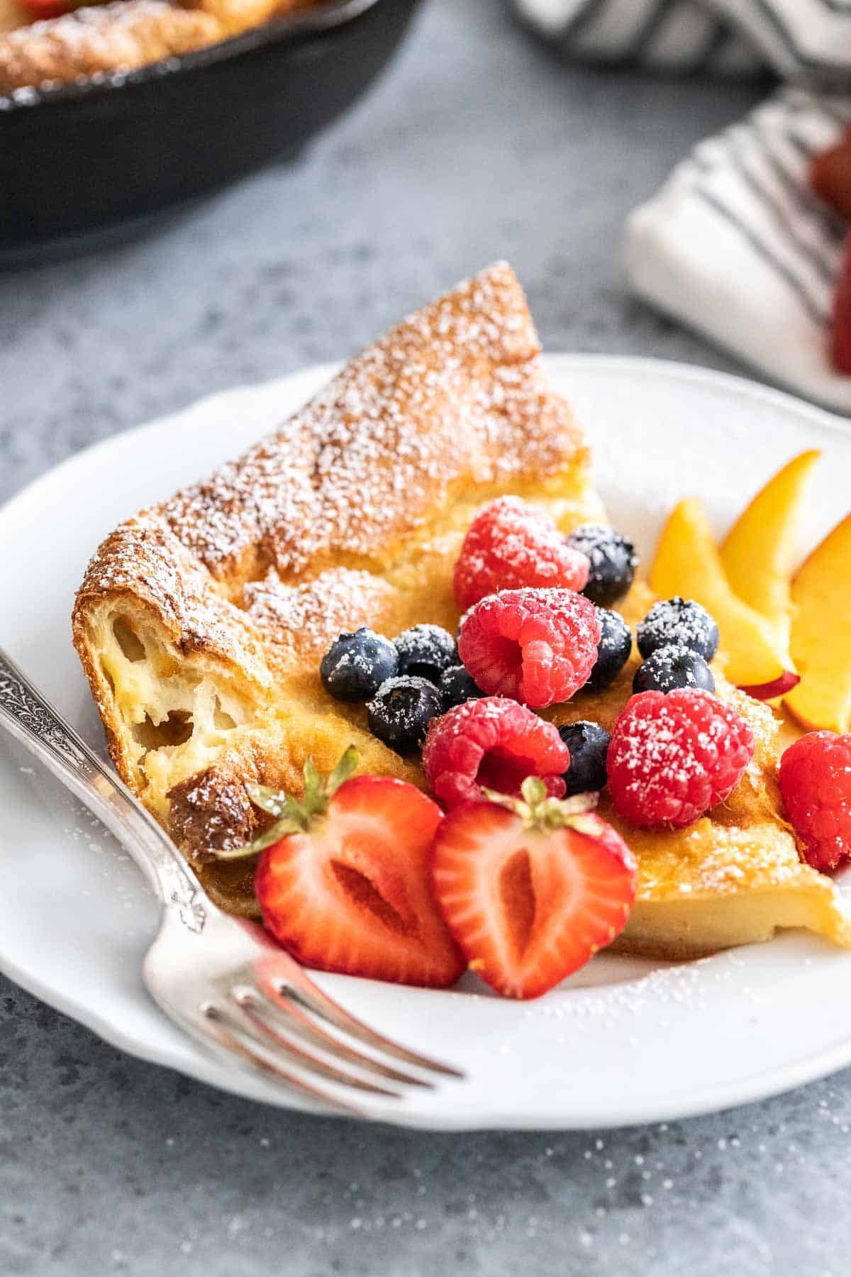 Une part de pancake néerlandais sur une assiette blanche garnie de fruits.